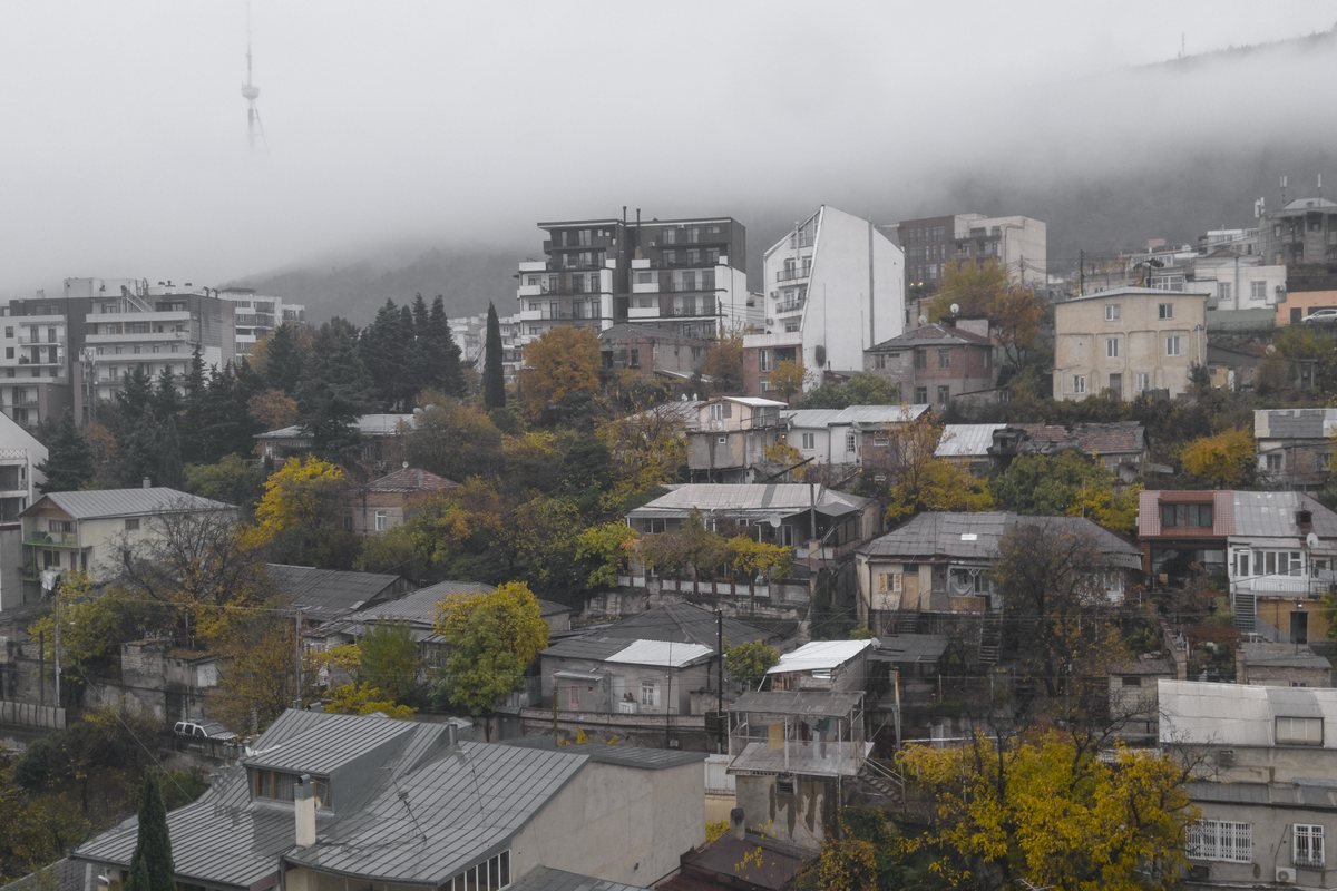 Casas y bloques de pisos del barrio de Vake, en Tbilisi, entre árboles otoñales y con niebla en las colinas